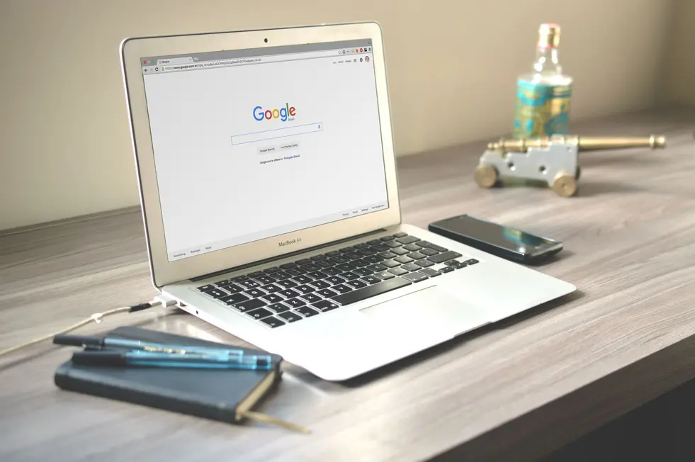 Notebook aberto com Busca Google moderna e plantas em mesa iluminada