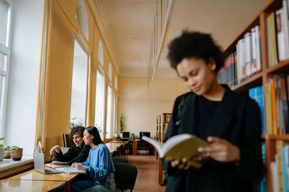 Pessoa sorrindo com laptop aberto no Google Acadêmico e livros acadêmicos