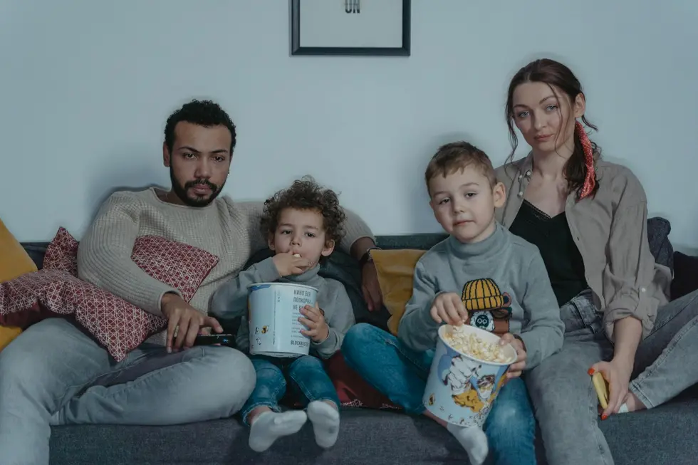 Família sorrindo na sala assistindo filme no streaming, com balde de pipoca